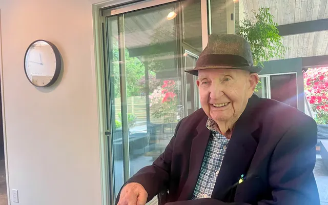 Bob Rummer in a hat, seated in front of the glass wall of one of his houses.